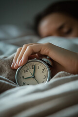 A woman is holding an alarm clock that is set to 7:00