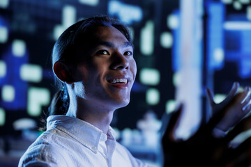Fototapeta premium Happy citizen wandering around city streets at night, looking around to surrounding skyscrapers in metropolitan cityscape setting. Businessman leaving work, taking a walk outside empty urban landscape