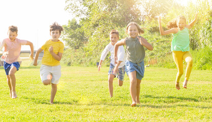 Portrait of five smiling preteen kids running in race and laughing in park