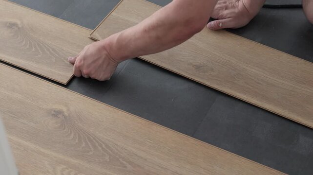 A close-up shot of hands carefully aligning and installing laminate flooring planks on a dark underlay