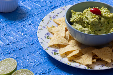 Beautiful blue table setting with guacamole in a bowl surrounded by nachos, cherry tomatoes and...