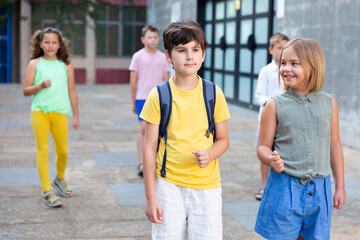 Positive tweenagers walking outside school building on summer day, going to home
