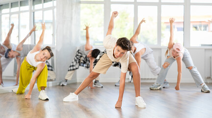 Obraz premium During workout, teenage student guy in dances with hip hop friends, learning to dance. Followers look closely at obscure teacher, follow instructions, repeat movements, dance elements