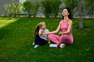 Fototapeta premium Mother and daughter practicing meditation on green grass in a peaceful outdoor setting