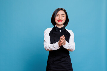 Smiling asian waitress wearing uniform applauding with to show support and appreciation portrait. Cheerful young attractive woman receptionist clapping hands and looking at camera