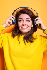 Caucasian woman is excited and wearing headphones while listening to music. Young brunette lady smiling and putting on a headset to listen to a song on an audio device, having fun with sounds.