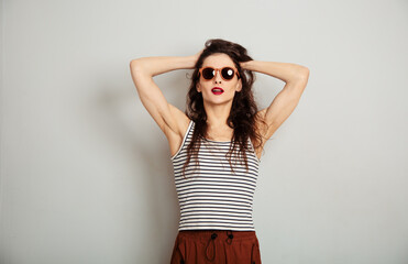 Naklejka premium Fun relax smiling woman posing in fashion sunglasses and white t-shirt with red lipstick on white wall background with empty copy space. Happy lifestyle