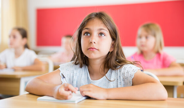 Diligent elementary school student tween girl studying with classmates, making notes of teacher lecture