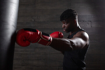 Powerful African American boxer wearing red gloves prepares to hit punching bag in gym showing his...