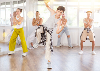 Positive teenage boy dancing hip-hop standing with her back to group members during workout session