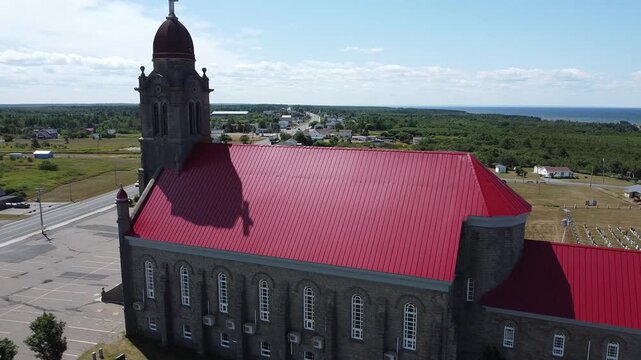 Survol de L'&Eacute;glise catholique romaine Saint-Simon et Saint-Jude, Grande-Anse avec un drone. Avec en arri&egrave;re-plan, le village, le cimeti&egrave;re, le quai et les vagues bleues de la Baie-des-Chaleurs.
