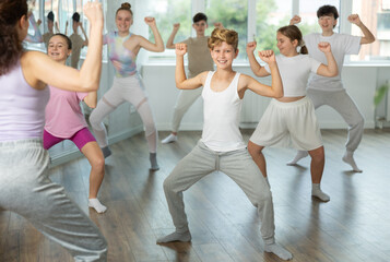 Fototapeta premium Guy teen performs modern dances repeats movements of unrecognizable teacher together with friends during lesson at choreographic school. Hobbies, active pastime