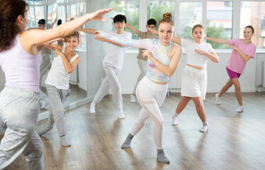 Fototapeta premium Young girls and boys repeat the movements of dance teacher, training in a spacious studio