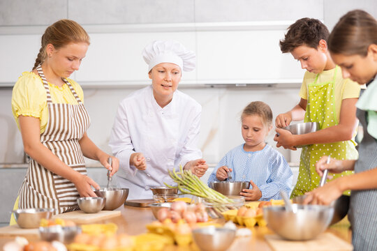 Adult woman chef at master class teaches group of children how to cook food