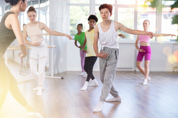 Focused teenager participating in beginner group ballet class, mimicking instructor dance moves with precision in sunlit choreography studio