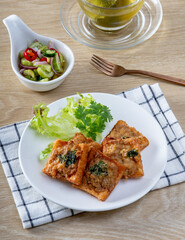 Fried Bread with Minced Pork Spread in white plate on the wooden table, traditional snacks and appetizers in Thailand