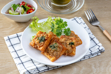 Fried Bread with Minced Pork Spread in white plate on the wooden table, traditional snacks and appetizers in Thailand