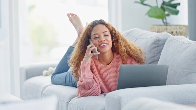A young woman talking on a phone and relaxing on the couch while using a laptop at home. Female freelancer lying on the sofa laughing, smiling while networking and working remotely from home