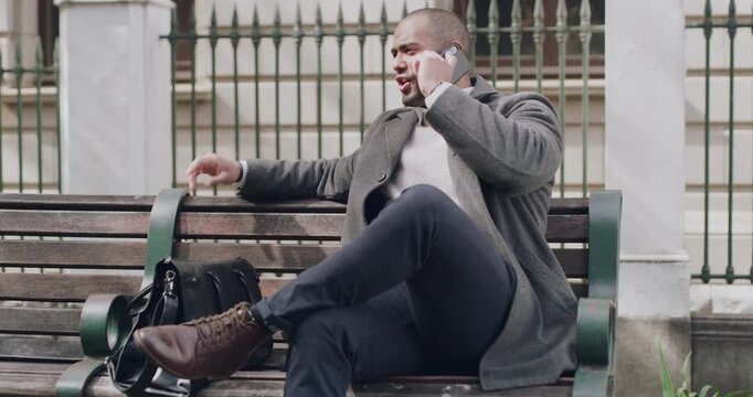 Trendy, stylish businessman on a phone call checking time, schedule or making business appointment and looking busy outdoors on a bench. A corporate professional man talking on a cellphone in a park