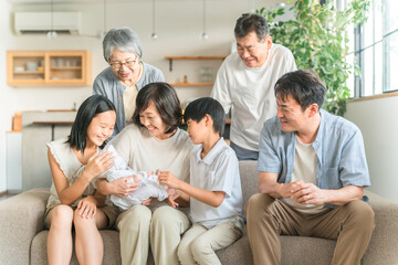 家のソファで赤ちゃんを抱っこするママと三世代家族・ファミリー
