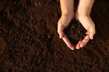 Man holding pile of soil outdoors, top view. Space for text
