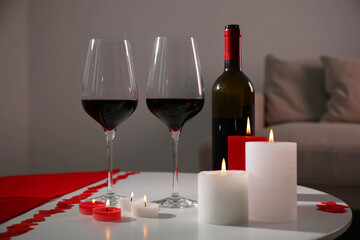 Burning candles, wine and paper hearts on table indoors