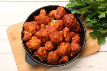 Baked cauliflower buffalo wings in baking dish and parsley on wooden table, top view