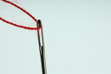 Sewing needle with red thread on white background