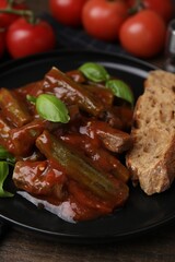 Tasty stew with okra, tomato sauce, bread and basil on wooden table, closeup