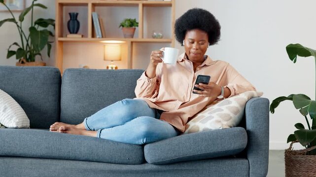 Laughing woman listening to music and sending a message with funny memes on her phone and drinking coffee while on the sofa. Happy black female browsing social media and surfing the internet online