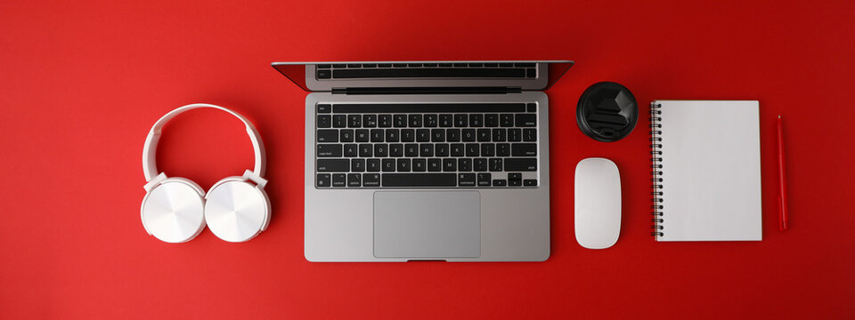A cup of coffee with headphones and a laptop on a red background