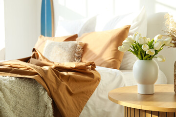 Vases with flowers and pampas grass on table in light bedroom, closeup