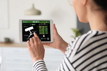 Young woman using smart home security system control panel in kitchen, closeup
