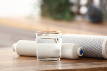 Glass of water with filters on wooden table in kitchen