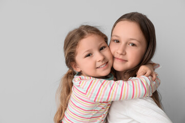 Cute little sisters hugging on light background, closeup