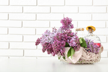 Basket with bottle of liquor and lilacs on white table near brick wall