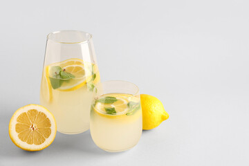 Glass and jug with fresh lemonade on grey background