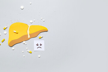 Yellow paper liver with gloomy face and pills on grey background