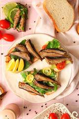 Plate of tasty sandwiches with canned smoked sprats on pink tile background