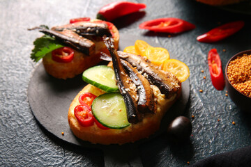 Board of tasty sandwiches with canned smoked sprats on black background