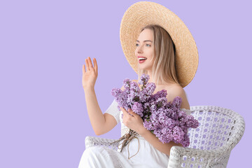 Young woman with lilac flowers in armchair on color background