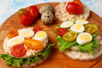 Rice crackers with quail eggs, tomatoes and lettuce on light blue background, closeup