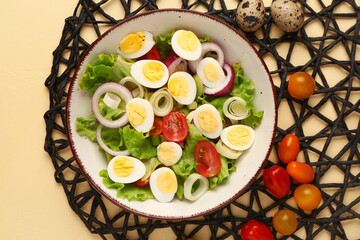 Tasty salad with quail eggs, tomatoes, onion and lettuce on beige background