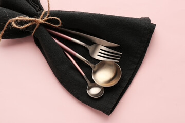 Stylish cutlery in black napkin on pink background