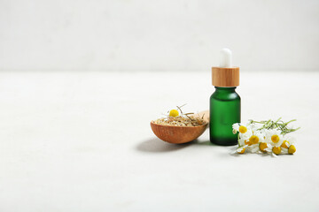 Bottle of essential oil, fresh and dried chamomile flowers on light background