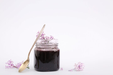 Jar with sweet jam, spoon and flowers isolated on white background