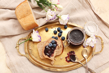 Tray with bread pieces, jar of blueberry jam and flowers on table, closeup