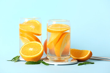 Glasses of infused water with orange slices on blue background
