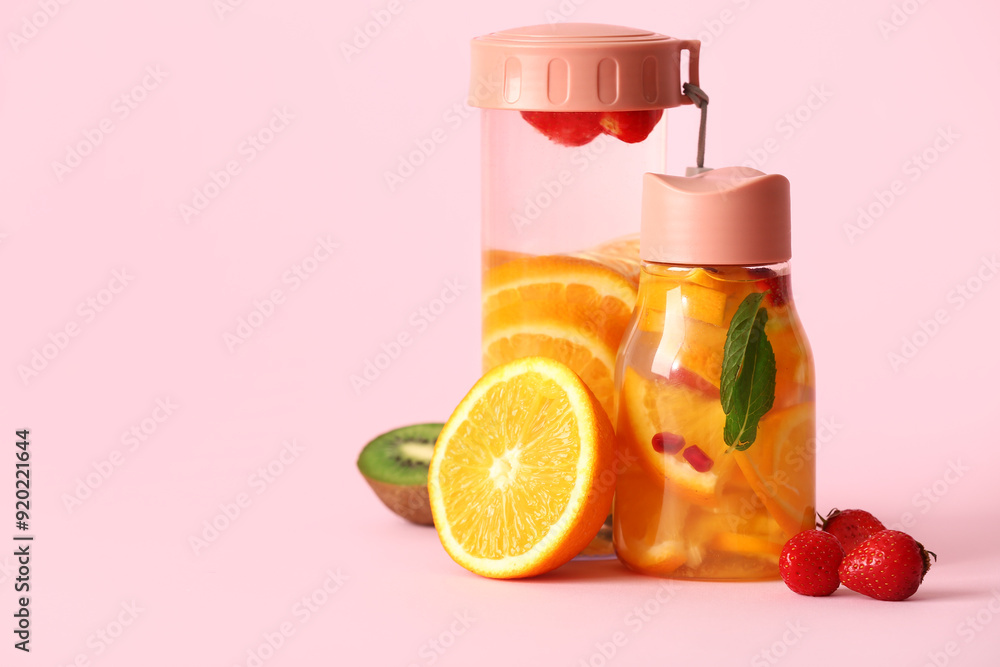 Wall mural sports bottles of infused water with different sliced fruits on pink background