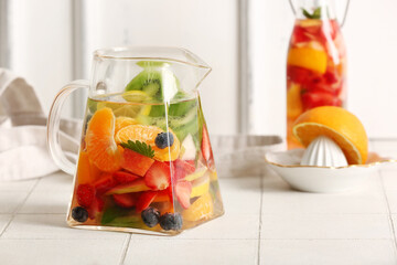 Jug and bottle of infused water with different sliced fruits on white tile table
